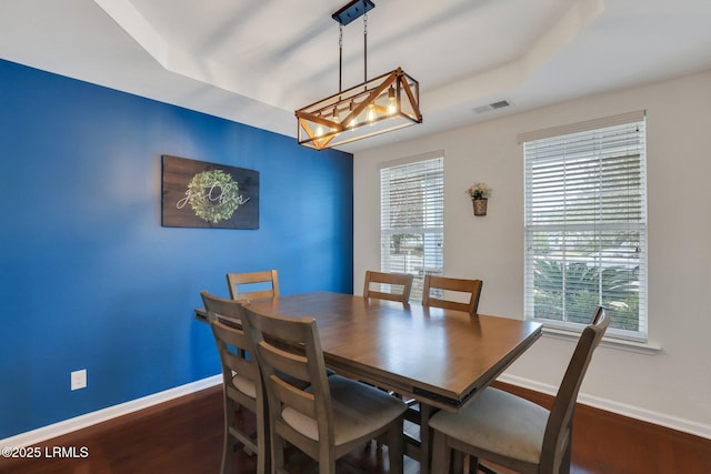 dining room featuring dark wood-style floors, baseboards, visible vents, and a tray ceiling