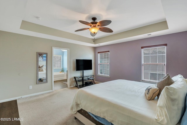 bedroom featuring carpet floors, a tray ceiling, ensuite bath, and baseboards