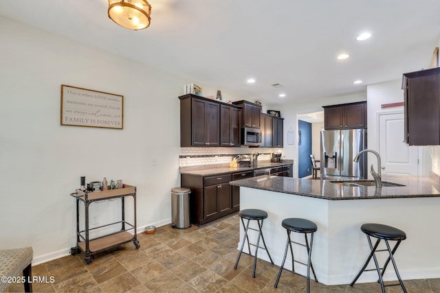 kitchen featuring appliances with stainless steel finishes, a sink, decorative backsplash, and a kitchen breakfast bar