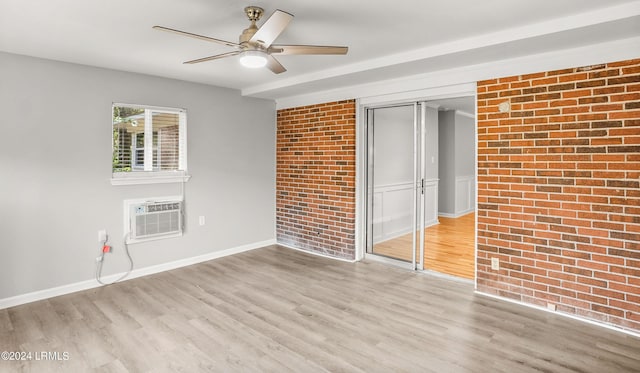 spare room with brick wall, light wood-type flooring, and an AC wall unit