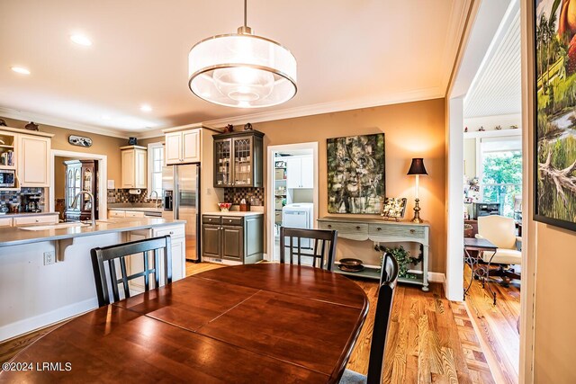 dining room with sink, ornamental molding, and light hardwood / wood-style floors