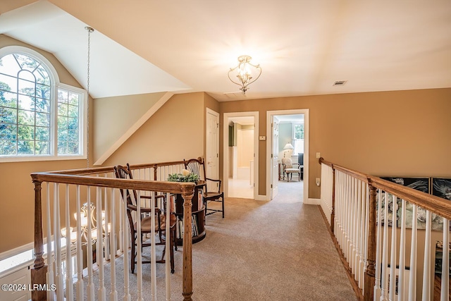 hallway with an inviting chandelier, lofted ceiling, and carpet flooring