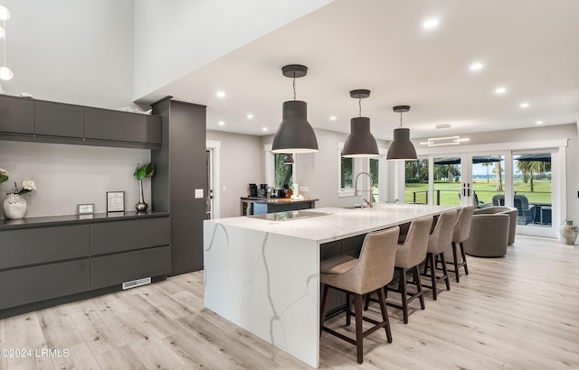 kitchen featuring decorative light fixtures, light hardwood / wood-style flooring, french doors, and a large island with sink