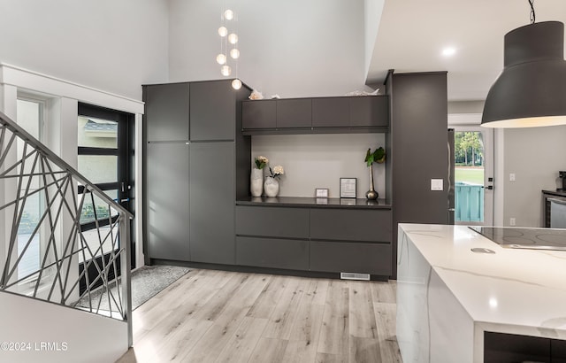 kitchen with black electric stovetop, light hardwood / wood-style floors, hanging light fixtures, and dark stone counters