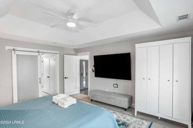 bedroom featuring a barn door, ceiling fan, and a tray ceiling