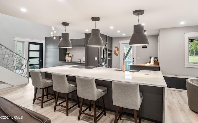 kitchen featuring a kitchen bar, fridge with ice dispenser, hanging light fixtures, light hardwood / wood-style flooring, and black electric stovetop