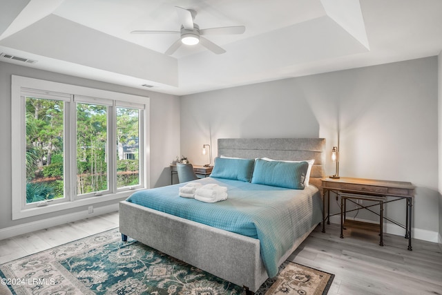 bedroom with a raised ceiling, ceiling fan, and light hardwood / wood-style flooring