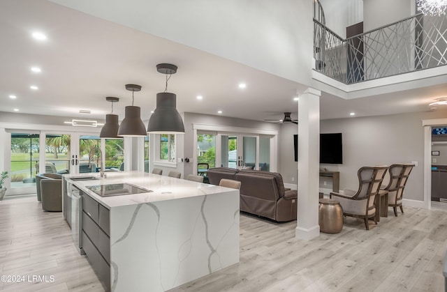 kitchen with a spacious island, sink, hanging light fixtures, stainless steel dishwasher, and light stone countertops