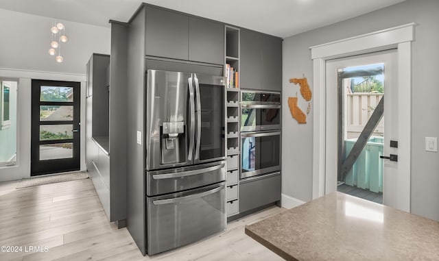 kitchen with gray cabinetry, light wood-type flooring, a healthy amount of sunlight, and appliances with stainless steel finishes