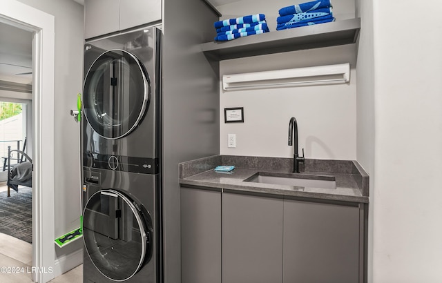 laundry area featuring stacked washer / dryer, light tile patterned flooring, sink, and cabinets