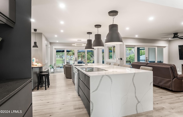 kitchen with a spacious island, light stone counters, light hardwood / wood-style flooring, black electric cooktop, and pendant lighting