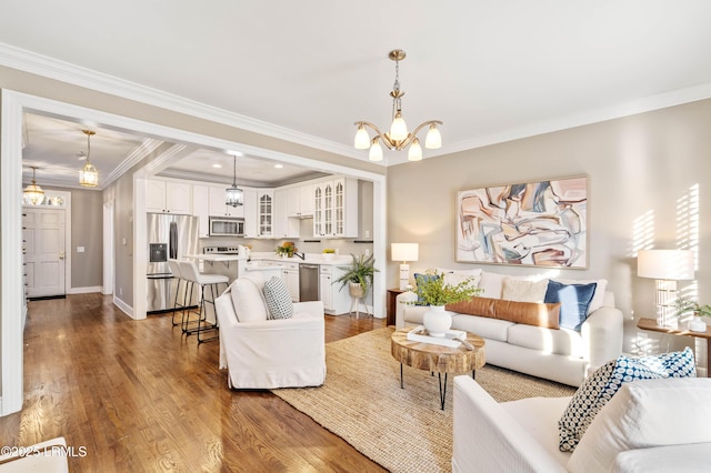 living area featuring an inviting chandelier, baseboards, ornamental molding, and wood finished floors