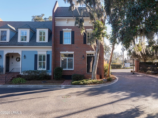 view of front of home with a shingled roof, a gate, and brick siding