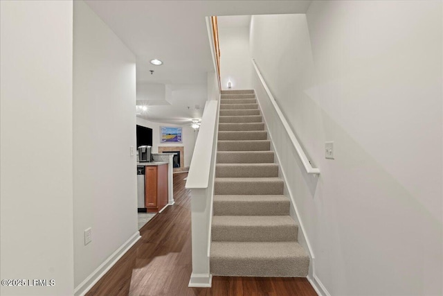 stairs with baseboards, wood finished floors, a fireplace, and recessed lighting