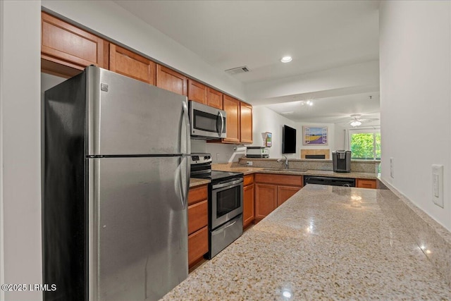 kitchen featuring recessed lighting, a sink, light stone countertops, brown cabinetry, and appliances with stainless steel finishes