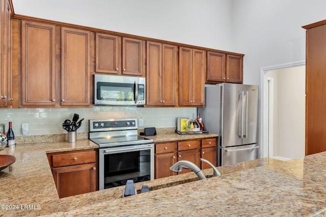 kitchen with stainless steel appliances, light stone countertops, sink, and backsplash