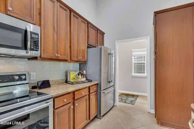 kitchen with tasteful backsplash, appliances with stainless steel finishes, light tile patterned floors, and light stone counters