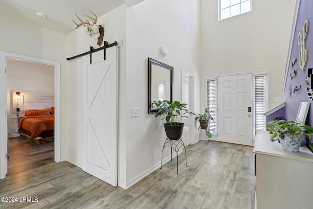 foyer entrance featuring a towering ceiling, a barn door, a healthy amount of sunlight, and light wood-type flooring