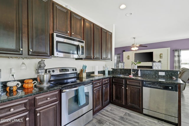 kitchen with sink, dark stone countertops, kitchen peninsula, stainless steel appliances, and light hardwood / wood-style floors