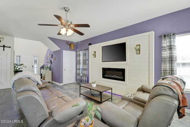 living room featuring ceiling fan, a large fireplace, a barn door, and light hardwood / wood-style flooring