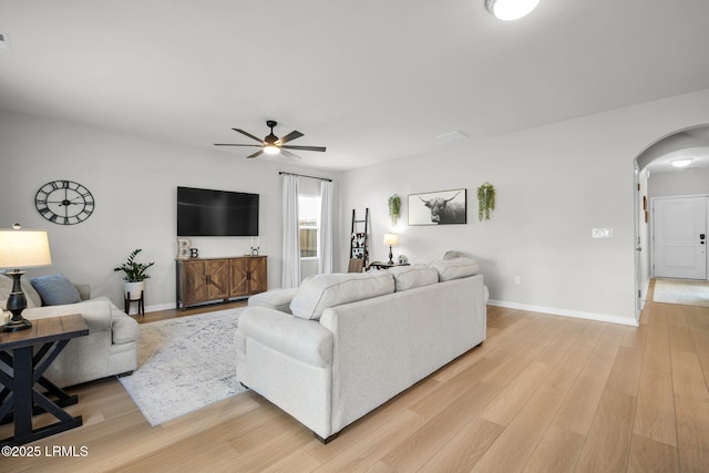 living area featuring light wood-type flooring, baseboards, arched walkways, and ceiling fan