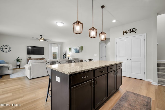 kitchen with a ceiling fan, pendant lighting, light wood-style flooring, and a kitchen bar