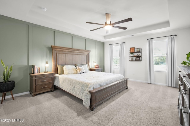 bedroom featuring a raised ceiling, light colored carpet, a decorative wall, a ceiling fan, and baseboards