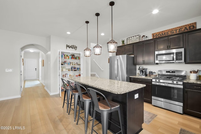 kitchen featuring arched walkways, appliances with stainless steel finishes, light stone counters, a center island, and light wood-style floors