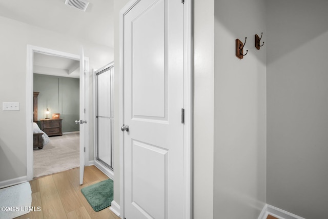 hallway with light wood-type flooring, a raised ceiling, visible vents, and baseboards