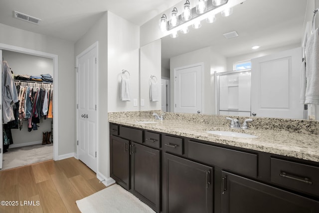 bathroom featuring double vanity, a stall shower, visible vents, wood finished floors, and a sink