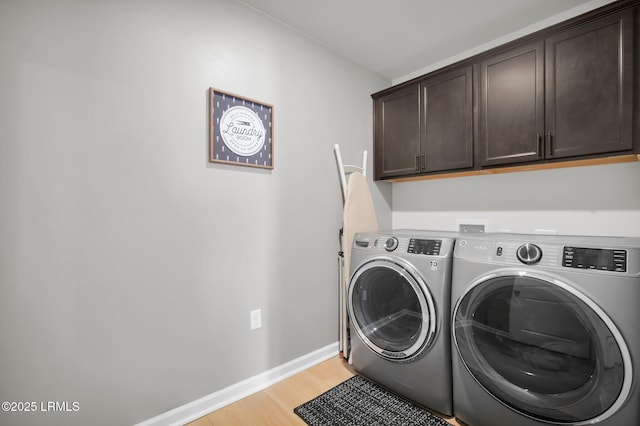 washroom with cabinet space, light wood-style flooring, baseboards, and washer and clothes dryer