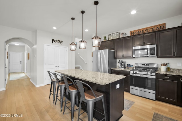 kitchen with light stone counters, stainless steel appliances, a kitchen island, light wood-type flooring, and a kitchen bar