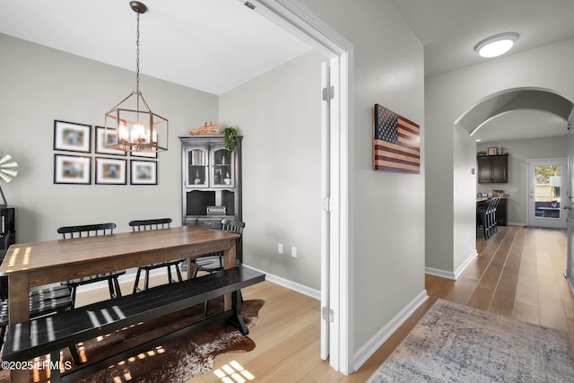 dining room with light wood finished floors, baseboards, arched walkways, and a notable chandelier