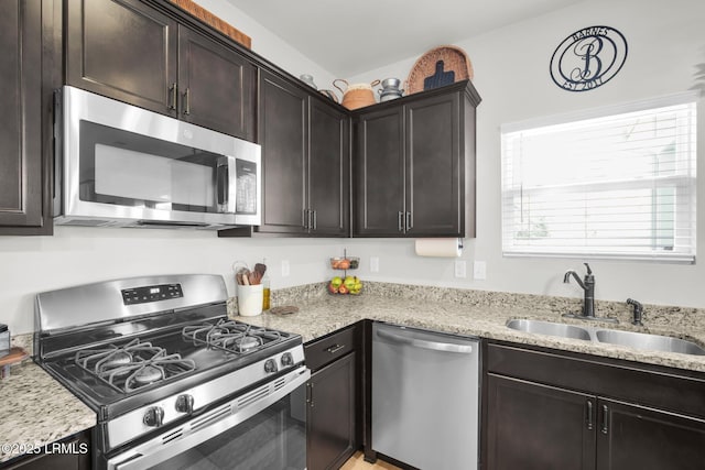 kitchen with light stone countertops, dark brown cabinets, stainless steel appliances, and a sink