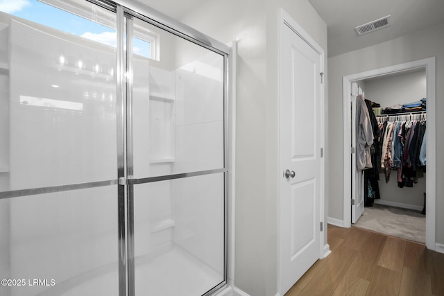 bathroom with a spacious closet, a stall shower, wood finished floors, and visible vents