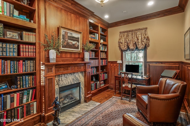 sitting room with a premium fireplace, wood-type flooring, built in features, and crown molding