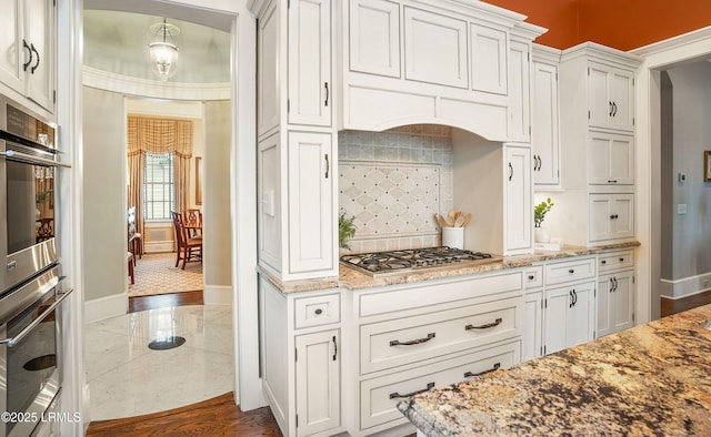 kitchen featuring pendant lighting, backsplash, light stone countertops, stainless steel gas cooktop, and white cabinets