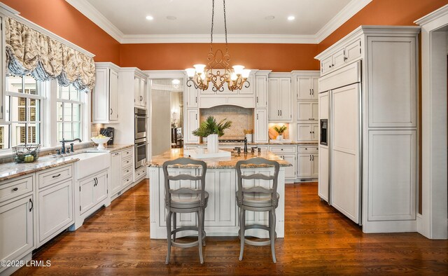 kitchen featuring sink, decorative light fixtures, a center island with sink, paneled fridge, and light stone countertops