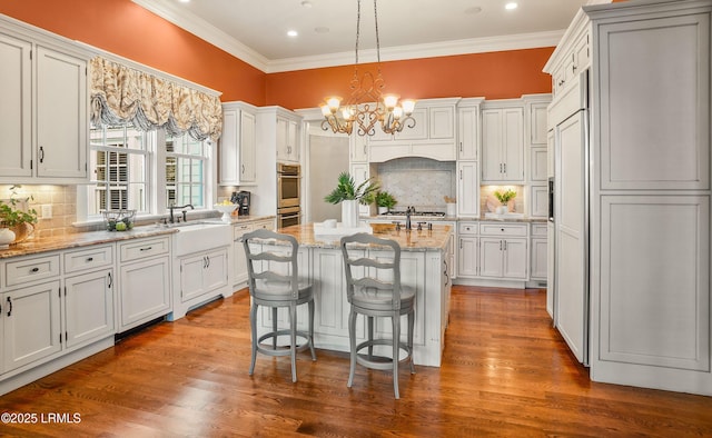 kitchen featuring sink, a breakfast bar area, a center island with sink, ornamental molding, and dark hardwood / wood-style flooring