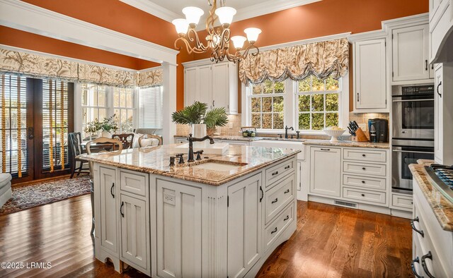 kitchen with pendant lighting, double oven, sink, ornamental molding, and a kitchen island with sink