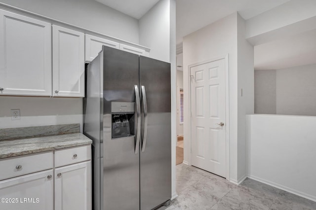 kitchen featuring stainless steel fridge, light stone countertops, and white cabinets