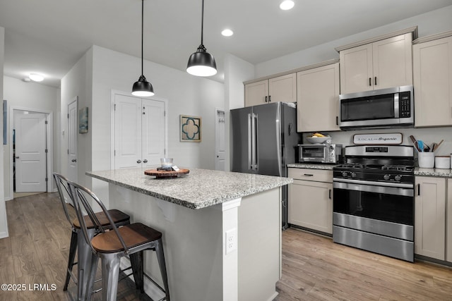 kitchen with stainless steel appliances, decorative light fixtures, light hardwood / wood-style floors, and a kitchen island