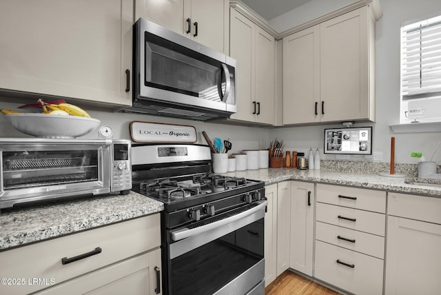 kitchen with appliances with stainless steel finishes, light stone countertops, and light hardwood / wood-style floors