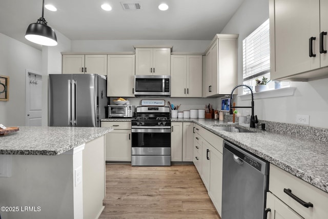 kitchen featuring sink, hanging light fixtures, light hardwood / wood-style flooring, appliances with stainless steel finishes, and light stone countertops