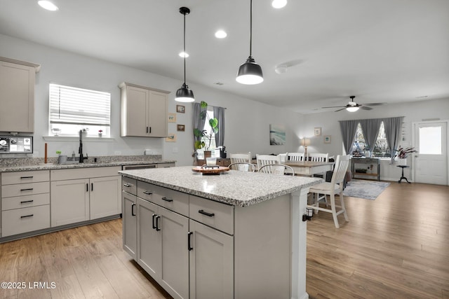 kitchen with decorative light fixtures, sink, a center island, light stone counters, and light hardwood / wood-style flooring