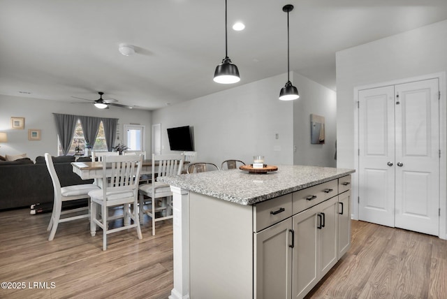 kitchen featuring pendant lighting, a center island, ceiling fan, light stone counters, and light wood-type flooring