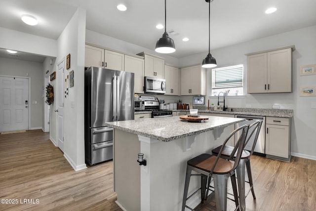 kitchen with sink, decorative light fixtures, a kitchen island, stainless steel appliances, and light stone countertops