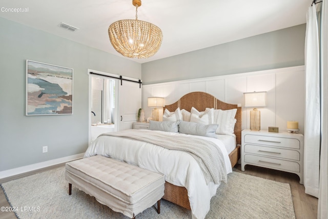 bedroom featuring connected bathroom, a barn door, a chandelier, and light hardwood / wood-style floors