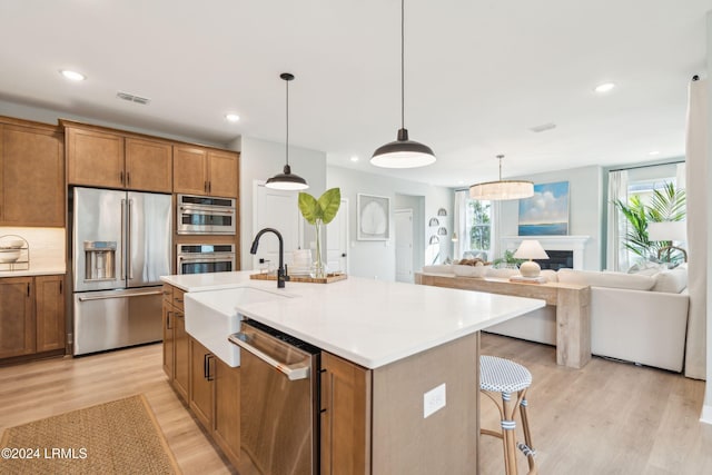 kitchen featuring sink, decorative light fixtures, a center island with sink, light wood-type flooring, and appliances with stainless steel finishes