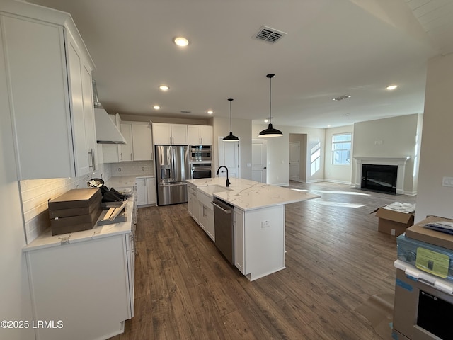 kitchen with white cabinetry, decorative light fixtures, an island with sink, stainless steel appliances, and light stone countertops